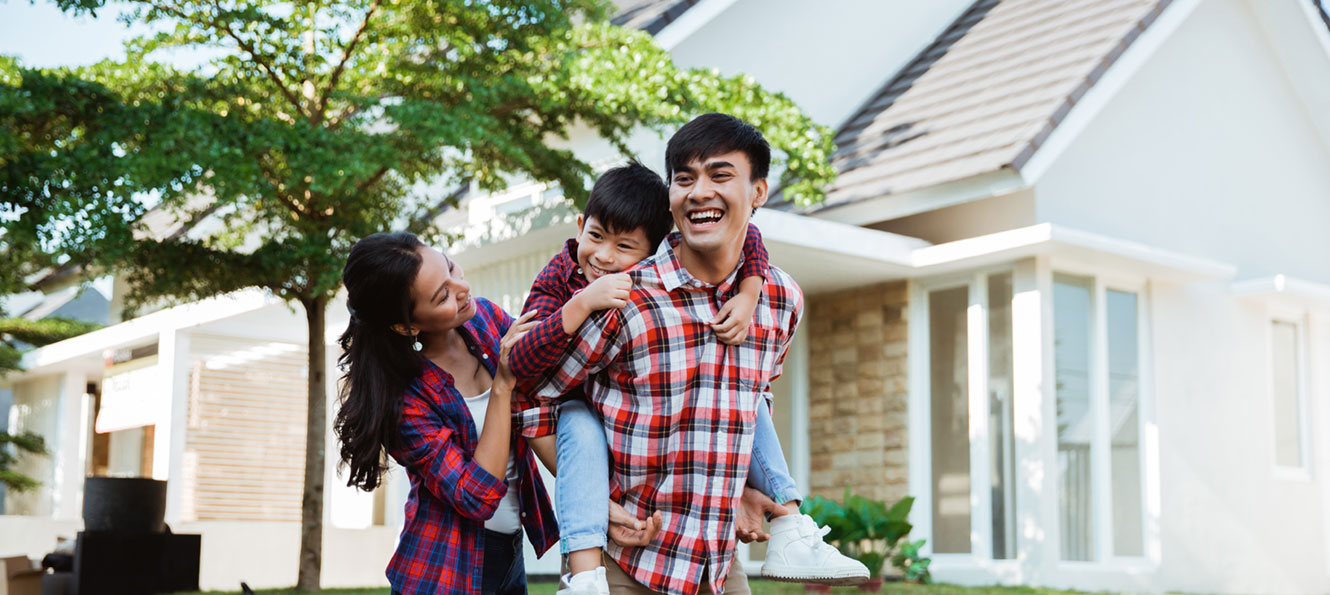 family of three standing outside their home, with a young child hugging dad