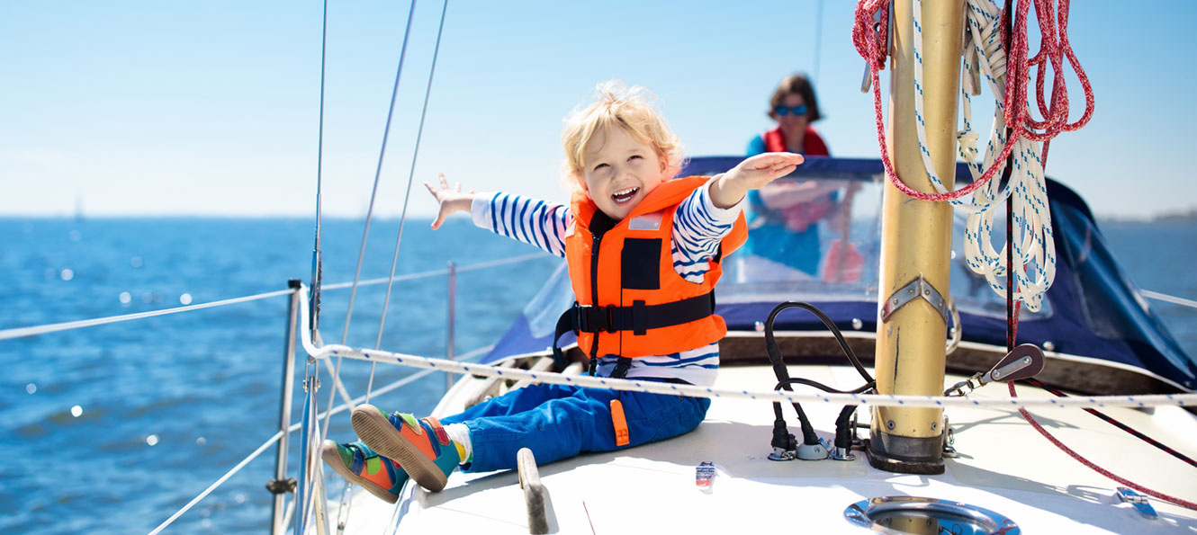 young child smiling and wearing a bright orange safety vest on the deck of a boat