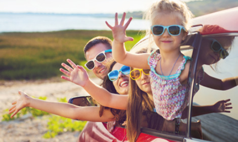 family of four wearing colorful sunglasses while hanging out of the car and waving