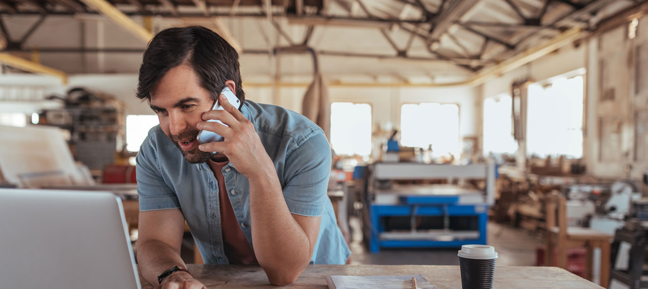 business owner talking on his cell phone in front of his laptop in a commercial facility shop