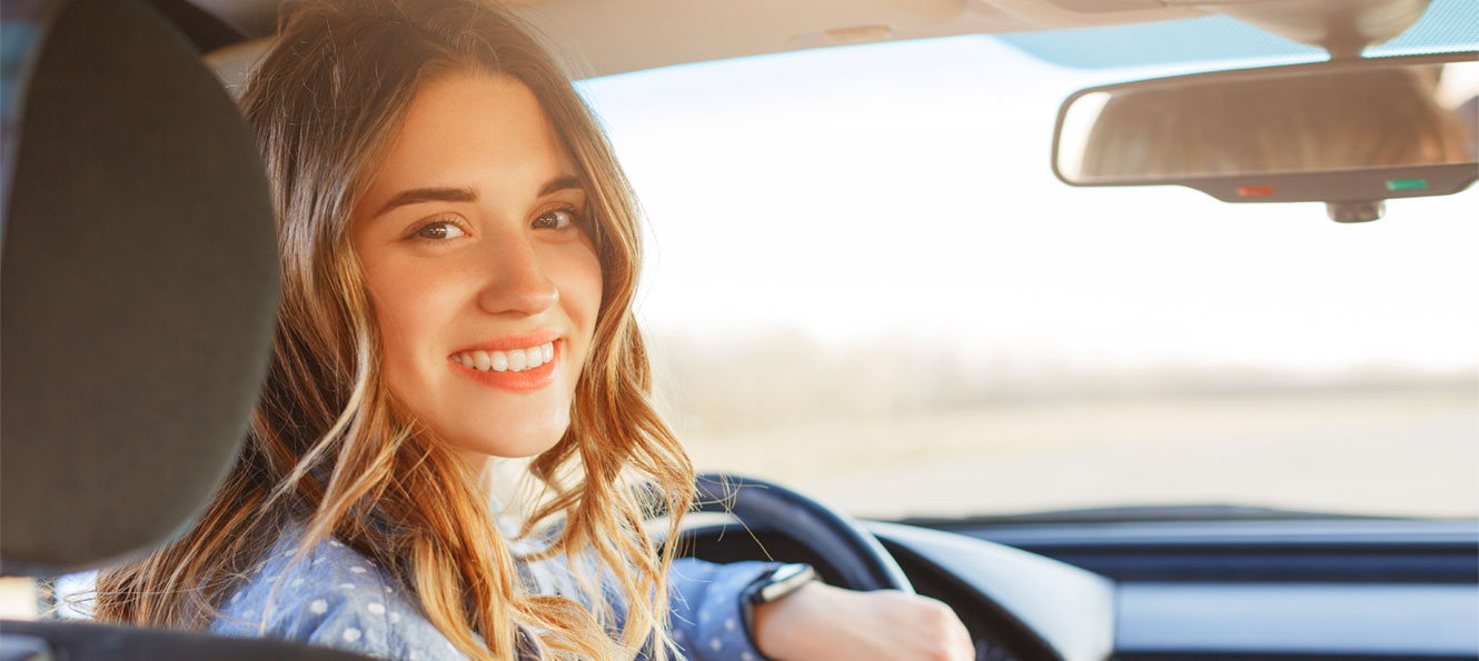 Young auto driver sitting in drivers seat and smiling while looking into the back seat