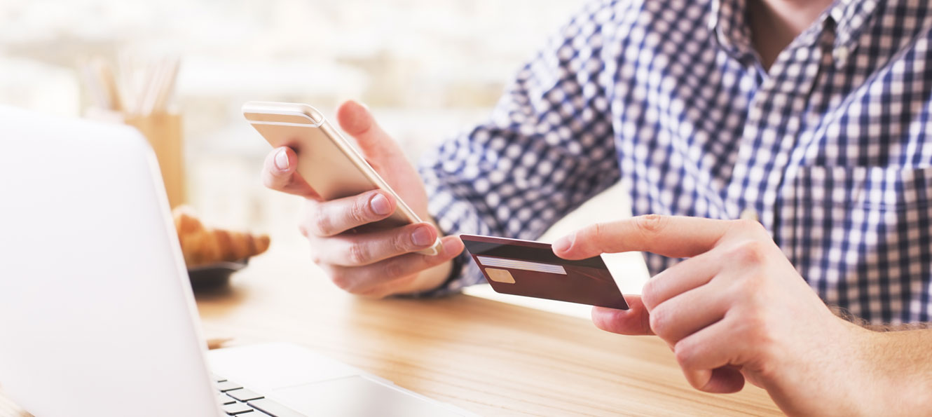 closeup of a person holding a bank card and a smartphone in front of a laptop