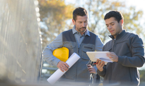business owner with a yellow hard hat talking to an employee outside