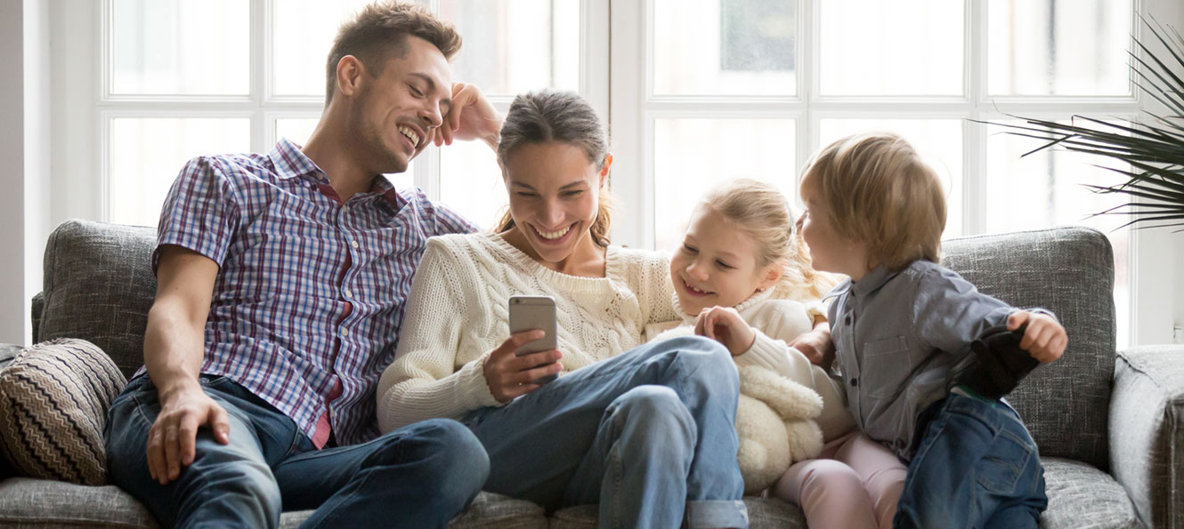 family of four sitting on a couch, smiling while mom looks at something on her smartphone