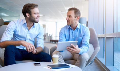 two businessmen sitting in an office lounge talking with a tablet in hand