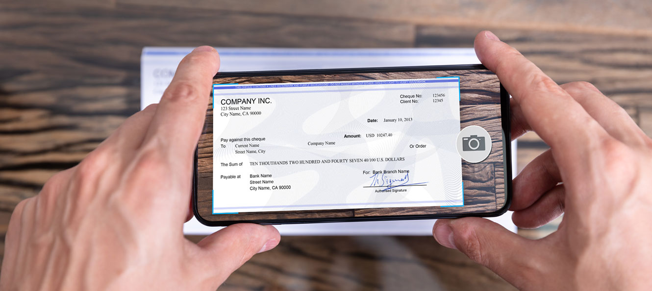 hands holding a smartphone, taking a picture of a printed check to deposit via a mobile app