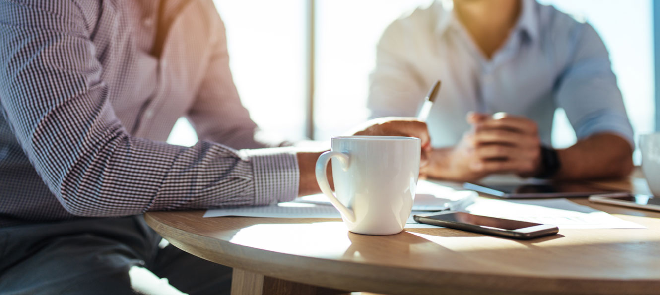 closeup of a coffee cup and cell phone on a table during a business meeting