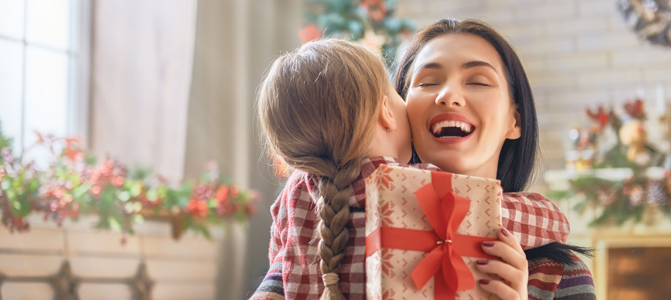 woman hugging a child while holding a gift in a holiday setting