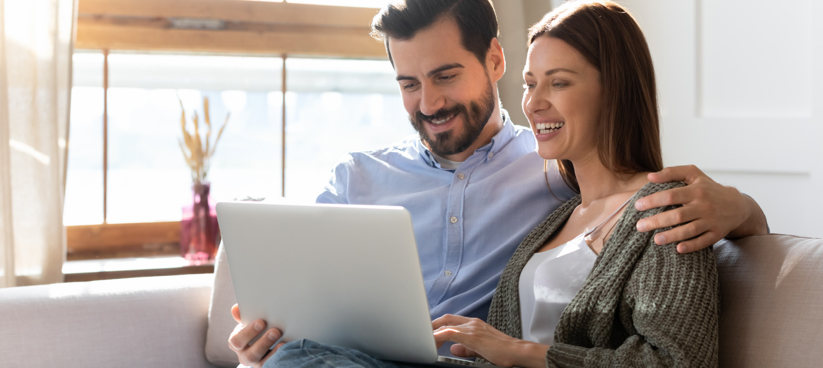 Couple sitting on couch looking at laptop smiling
